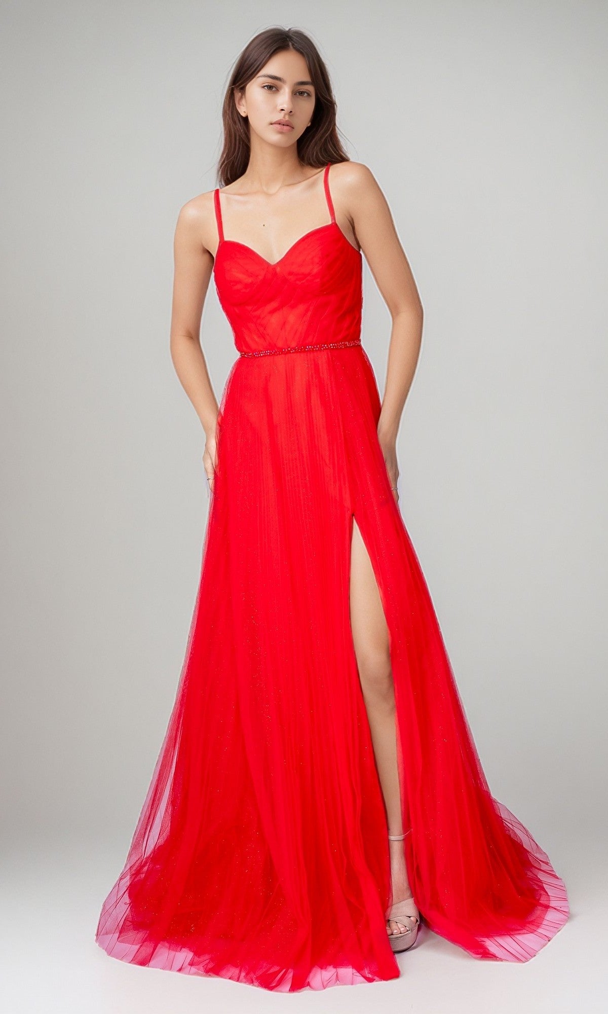 A woman poses in a studio wearing the Long Formal Dress: Nina Canacci 5401—a bright red gown with thin straps, fitted bodice, and high slit—paired with strappy heels.